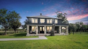 A two-story house with a balcony, large windows, and a well-maintained lawn. - Charming Farmhouse W/hot-tub Near 290 Wine Trail (Fredericksburg)