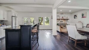 A spacious kitchen with a central island, white cabinetry, and a dining area with a table and chairs. - Charming Farmhouse W/hot-tub Near 290 Wine Trail (Fredericksburg)