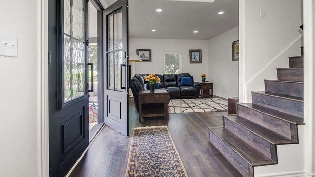 A spacious living room with a dark wood staircase, a black door, and a patterned rug. - Charming Farmhouse W/hot-tub Near 290 Wine Trail (Fredericksburg)