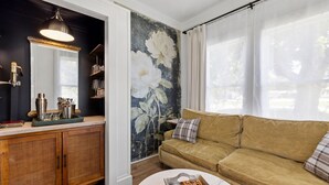 En stue med sofa, sofabord, skab og et stort blomsterdekorativt vægmaleri.