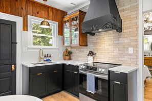 Une cuisine moderne avec des meubles de couleur noire, une cuisinière en acier inoxydable et une fenêtre donnant sur les arbres.