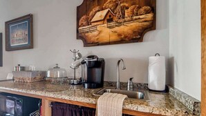 A kitchen with granite countertops, a coffee maker, a sink, and a painting of a rural scene. - The Manor Haus at Messina Hof Hill Country Winery-presidents (Fredericksburg)