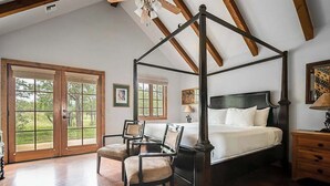 A bedroom with a four-poster bed, wooden flooring, and a large window with a view of greenery. - The Manor Haus at Messina Hof Hill Country Winery-presidents (Fredericksburg)