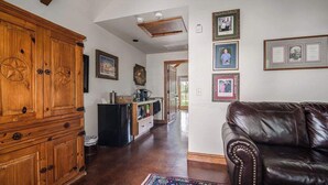 A spacious living area with a wooden cabinet, a black leather couch, and a kitchen in the background. - The Manor Haus at Messina Hof Hill Country Winery-presidents (Fredericksburg)