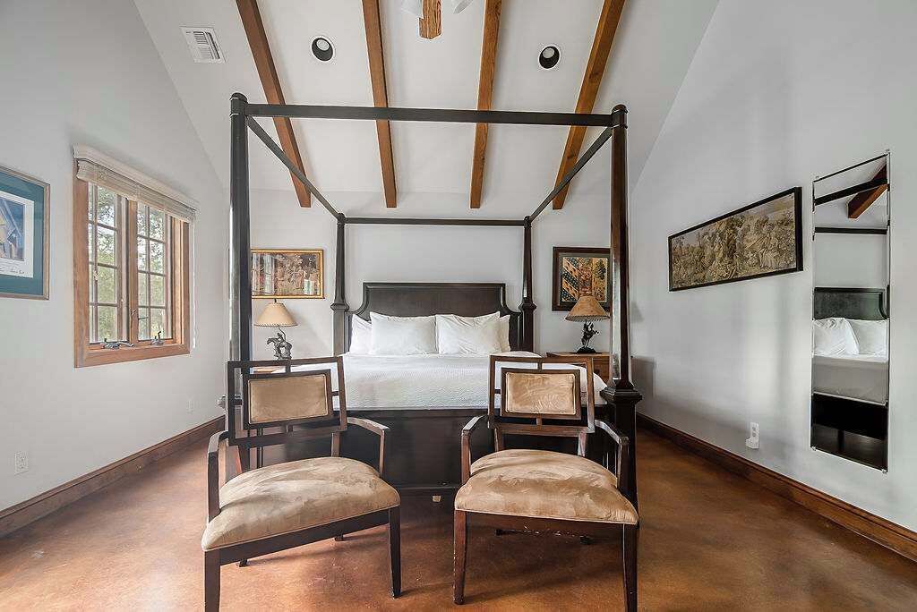 A bedroom with a four-poster bed, two chairs, a nightstand, and a bedside table.