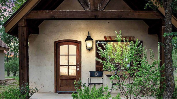A rustic building with a wooden front door, a small porch, and a well-maintained garden. - The Manor Haus at Messina Hof Hill Country Winery-presidents (Fredericksburg)