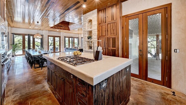 A spacious kitchen with a large island, wooden cabinets, and a stone fireplace. - Luxury Lakefront Escape on Lake Travis (Marble Falls)