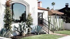 Una casa moderna con un amplio ventanal de arco, una escalera y una variedad de cactus y plantas de agave en el jardín.