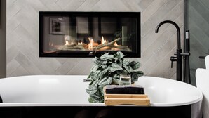 Un baño moderno con una bañera independiente, una planta grande en maceta y una chimenea sobre la bañera.