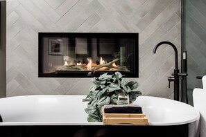 A modern bathroom with a freestanding bathtub, a large potted plant, and a fireplace above the tub. - Award-Winning Balboa Park Home w/ Hot Tub Near Zoo (San Diego)