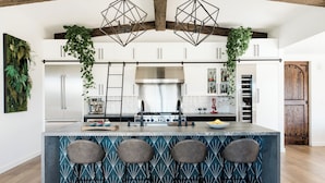 Una cocina moderna con una isla central, taburetes de bar, plantas colgantes y techo de madera.