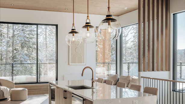 A modern kitchen with a large island, pendant lights, and a view of snowy trees through large windows. - Chalet Symbiose21 - Spa& Sauna& Ski (Saint-Come)