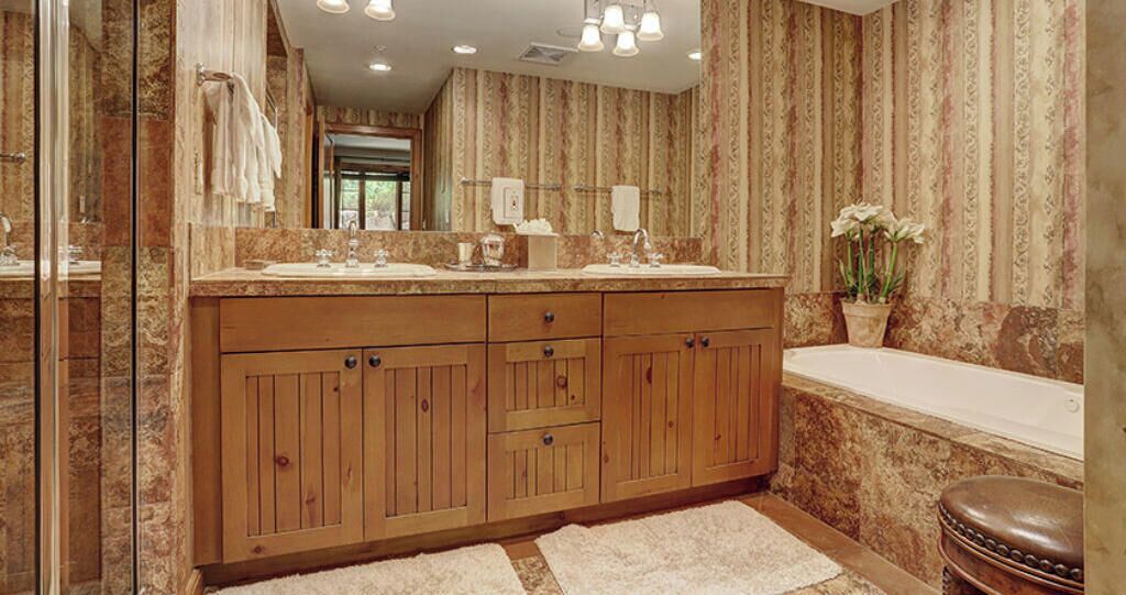 A bathroom with wooden cabinets, a marble countertop, a bathtub, and a mirror.