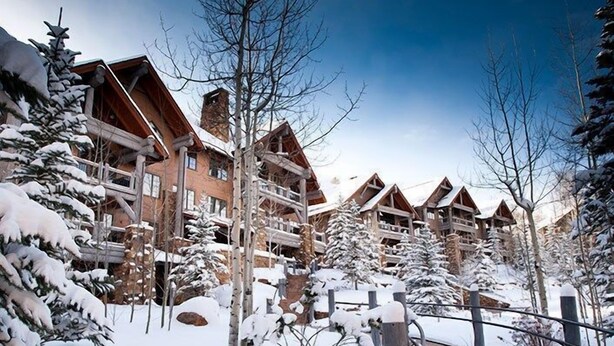 Een met sneeuw bedekte lodge met meerdere houten gebouwen, een pad van stenen en sneeuwzware bomen.