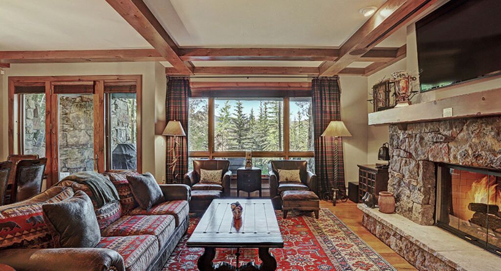 A cozy living room with a stone fireplace, a large window with a forest view, and a comfortable seating area with a coffee table.