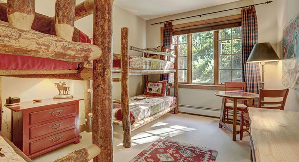 A rustic room with a bunk bed, a wooden dresser, a round table, and a chair.