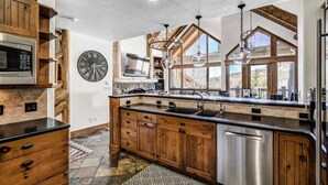 A modern kitchen with wooden cabinets, a large island, stainless steel appliances, and a stone backsplash.