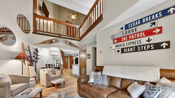 Een ruime woonruimte met een hoge plafond en een trap. Borden wijzen op voorzieningen zoals 'CEDAR BREAKS', 'Lodge', 'SKI PATROL', 'NAVAJO EXPRESS' en 'GIANT STEPS'.