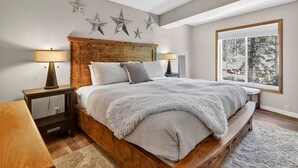 Een slaapkamer met een houten bed, een groot raam met uitzicht op bomen en sterren decoraties aan de muur.