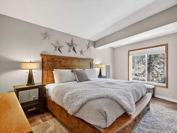 A bedroom with a wooden bed frame, a large window with a view of trees, and star decorations on the wall.