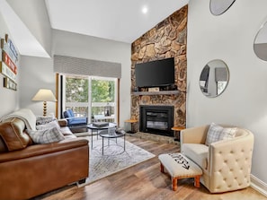 A modern living room with a stone fireplace, leather sofas, and a large TV.