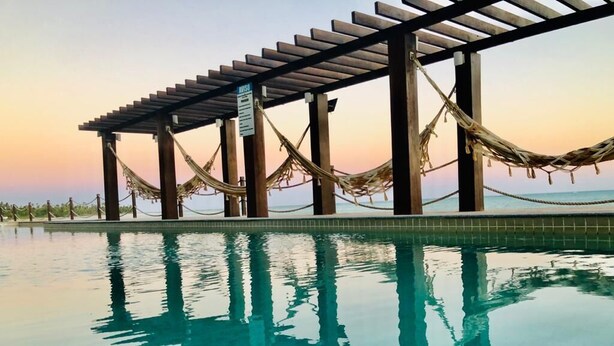 Una piscina con un pérgola de madera y hamacas.