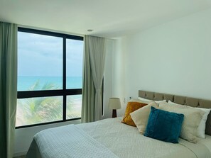 A hotel room with a large window offering a view of the ocean and palm trees. - Apartment with an ocean view in Maceió (Maceió)