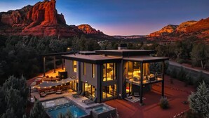 A modern house with a pool, large windows, and a view of red rock formations.