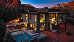 A modern two-story house with a pool, large windows, and a view of red rock formations.