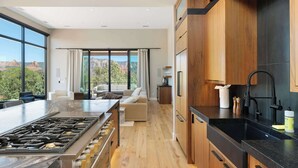 A modern kitchen with a large island, wooden cabinets, and a view of the mountains.