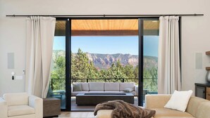 A modern living room with a large sliding glass door leading to a balcony with a mountain view.