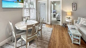Ein Wohnzimmer mit rundem Tisch, Stühlen, einer Couch, einem Fernseher und einer Tür zu einem weiteren Raum.