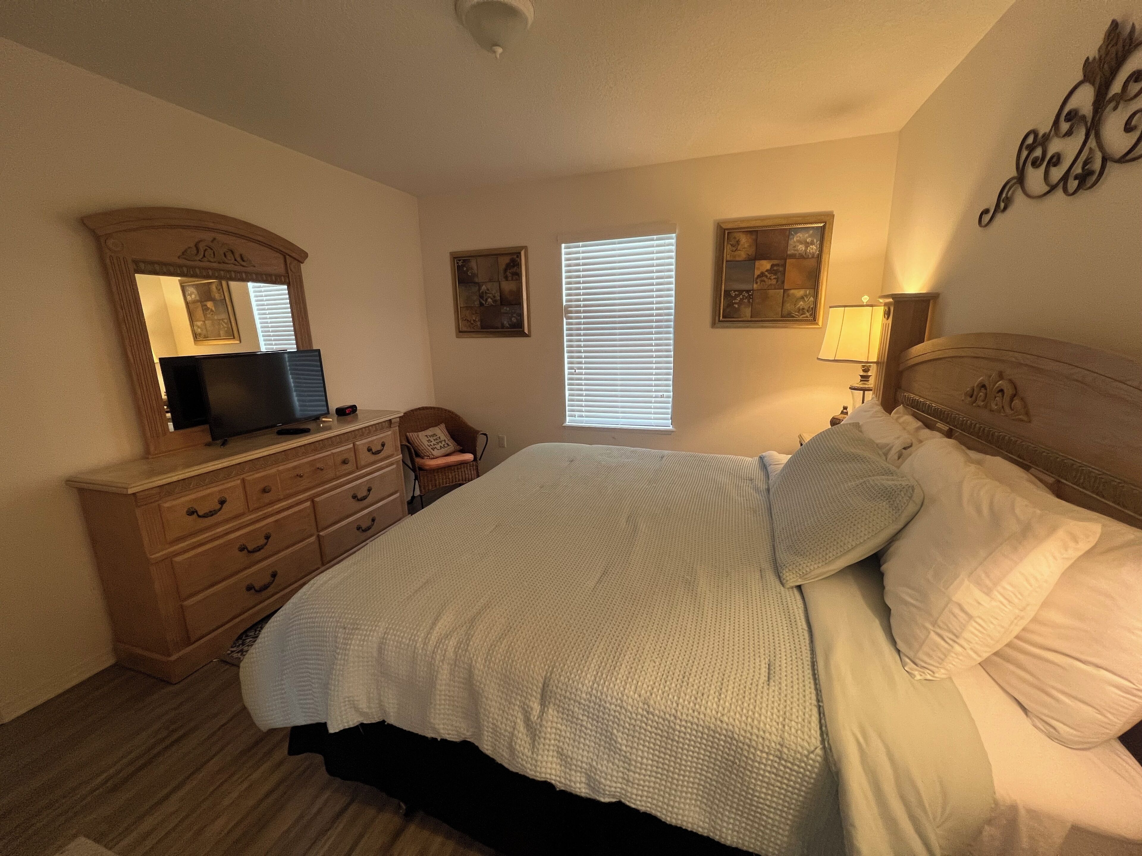 Un dormitorio con cama, cómoda, televisor y obras de arte en las paredes.