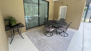 Varanda coberta com mesa, cadeiras, ventilador de teto e porta de correr de vidro.
