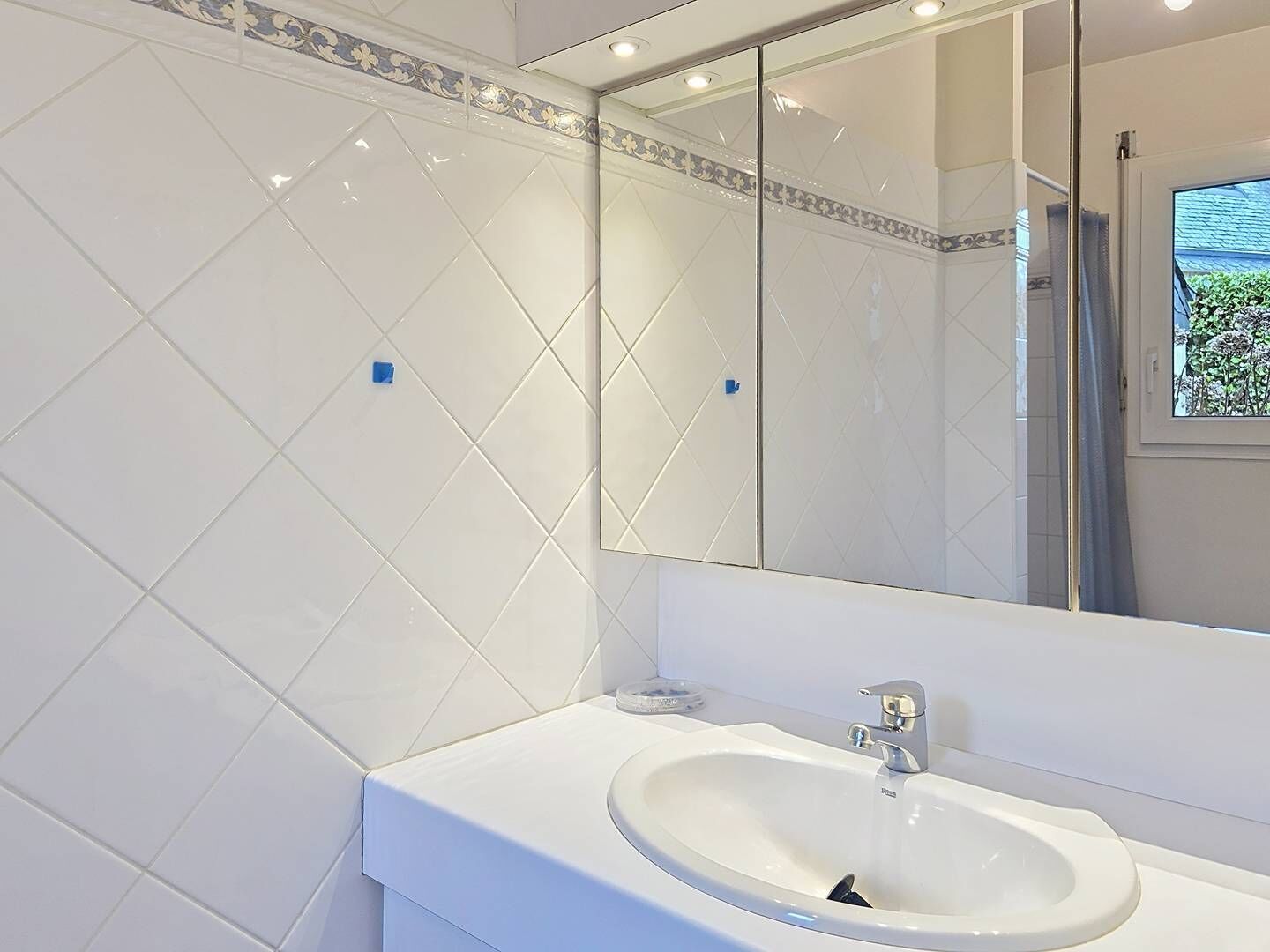 A modern bathroom with a white sink, a large mirror, and a shower visible through a glass door.