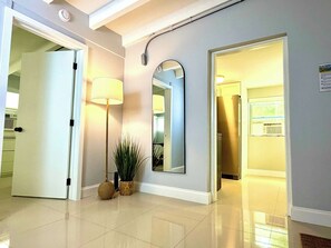 A hallway with a polished floor, a lamp, a mirror, and a door leading to a room. - 1 Bedroom on the Barrier Island. Walk to the Beach (Fort Lauderdale)