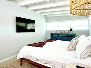 A modern bedroom with a bed, a television mounted on the wall, a blue dresser, and a window with natural light. - 1 Bedroom on the Barrier Island. Walk to the Beach (Fort Lauderdale)