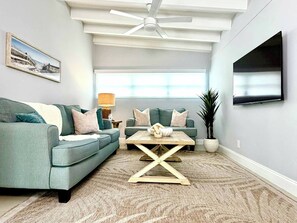 Ein Wohnzimmer mit Deckenventilator, zwei Sofas, einem Couchtisch, einer Lampe und einem an der Wand montierten Fernseher.