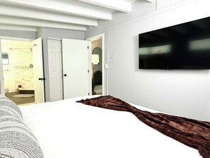 A hotel room with a bed, a TV mounted on the wall, a bathroom visible through an open door, and a patterned throw blanket on the bed. - 1 Bedroom on the Barrier Island. Walk to the Beach (Fort Lauderdale)