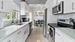 A modern kitchen with white cabinets, stainless steel appliances, a dining area with a table and chairs, and a pendant light above the sink. - 2 Bedroom on the Barrier Island. Walk to the Beach (Fort Lauderdale)