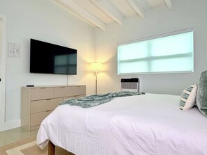 Ein Schlafzimmer mit einem Bett, einem Fernseher, einer Lampe und einem Fenster.