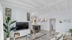 A modern living room with a flat-screen TV, a glass coffee table, a sofa, and a dining area with chairs. - 2 Bedroom on the Barrier Island. Walk to the Beach (Fort Lauderdale)