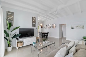 A modern living room with a flat-screen TV, a glass coffee table, a sofa, and a dining area with chairs. - 2 Bedroom on the Barrier Island. Walk to the Beach (Fort Lauderdale)