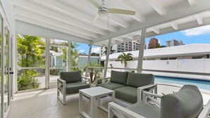 A sunlit outdoor lounge area with a pool view, featuring a ceiling fan, white furniture, and glass doors leading to a poolside. - 2 Bedroom on the Barrier Island. Walk to the Beach (Fort Lauderdale)