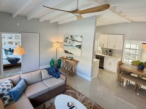 Un salon moderne comprenant un canapé, une table à manger et un coin cuisine avec des meubles blancs et un ventilateur de plafond.
