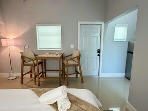 Une chambre d’hôtel avec un lit, deux chaises, une table, une lampe et une porte.
