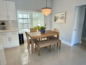 A modern kitchen with white cabinets, a coffee machine, and a dining area with a wooden table, chairs, and a bench. - 3 Bedroom on the Barrier Island. Walk to the Beach (Fort Lauderdale)