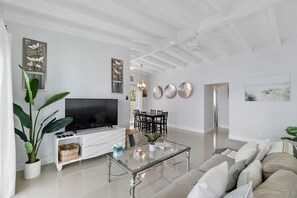 Ein modernes Wohnzimmer mit Flachbildfernseher, Glastisch, einer Couch und einem Essbereich mit Stühlen.