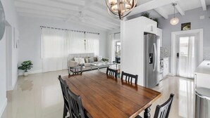 A spacious living area with a wooden dining table, a sofa, and a kitchen in the background. - Entire Villa (3 Units) on the Barrier Island (Fort Lauderdale)