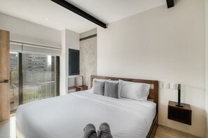 A modern bedroom with a large bed, a nightstand, a wall-mounted TV, and a balcony with a view of buildings. - Myla - 1BR - Roma Norte - Piso Alto (Mexico City)